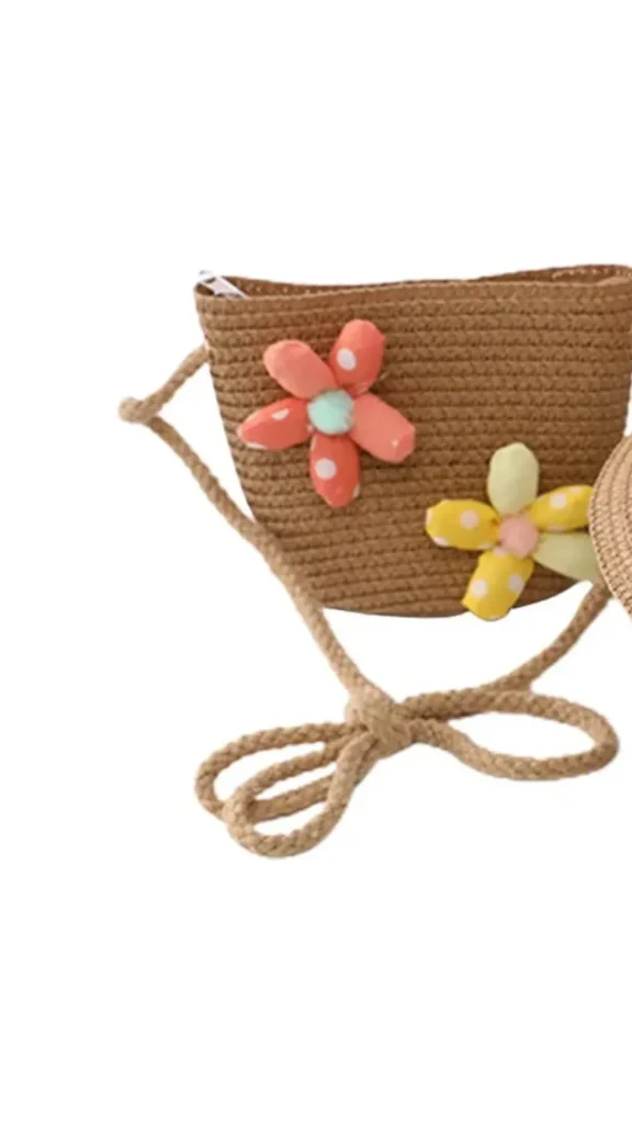 An image from file 1 (1)_4.webp showing a matching kids' straw summer accessories set on a plain white background. The set includes a light brown woven straw sun hat with a wide brim, tied with a white satin ribbon bow and decorated with two plush fabric flowers—one orange and one yellow with white polka dots. Next to it sits a matching small woven straw crossbody purse with a twisted rope strap, adorned with the same orange and yellow polka-dot fabric flowers.