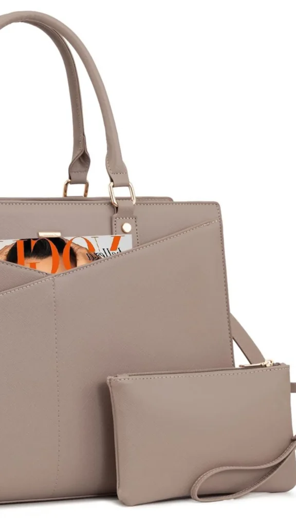 An image from file "1_18.webp" showing a close-up shot of a professional taupe-grey faux leather laptop handbag and a matching small zippered wristlet pouch against a white background. The tote bag features top handles attached with rectangular gold rings, a structured design, and an angled front slip pocket containing a magazine. The small wristlet pouch is positioned in front of the tote bag, featuring a top zipper with gold hardware and a slim wrist strap.