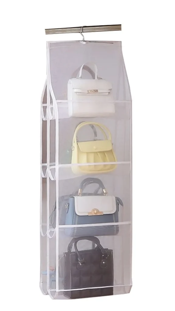 An image from file "2_19.webp" showing a space-saving, hanging handbag organizer suspended from a closet rod. The organizer is made of a semi-transparent white mesh fabric with structured, open-sided shelves designed to store multiple bags vertically. It is neatly arranged with four structured handbags: a white top-handle bag on the top shelf, a light yellow pleated handbag on the second, a two-tone blue and white satchel on the third, and a quilted black tote bag on the bottom shelf. The entire display is set against a plain white background.