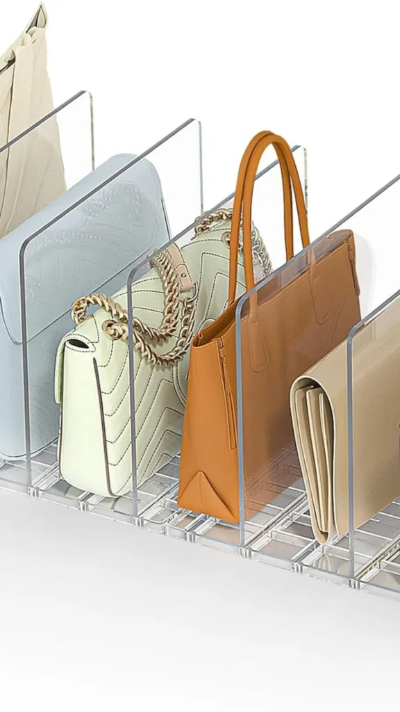 A product photograph from 5_6.webp showing a clear acrylic closet shelf organizer designed to store handbags upright. The clear plastic divider rack separates several purses neatly into slots. The bags on display include a light blue flap bag, a pale mint green quilted crossbody with a gold chain strap, a structured tan leather tote bag with tall top handles, and a folded beige leather envelope clutch, all set against a clean white background.